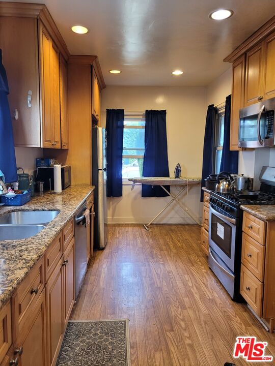 kitchen with light stone countertops, light hardwood / wood-style flooring, stainless steel appliances, and sink