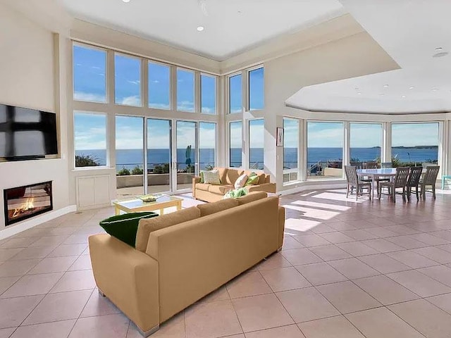 living room featuring a water view, a towering ceiling, light tile patterned flooring, and a wealth of natural light