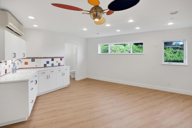 kitchen featuring white cabinets, ceiling fan, light hardwood / wood-style floors, and an AC wall unit