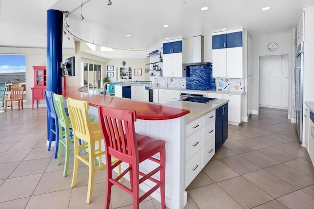 kitchen featuring a breakfast bar area, wall chimney exhaust hood, white cabinets, and a center island with sink