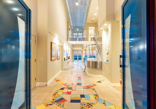 hallway featuring a towering ceiling, light tile patterned floors, and elevator