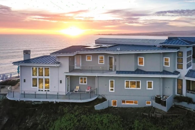 back house at dusk with a water view, a balcony, and central AC unit