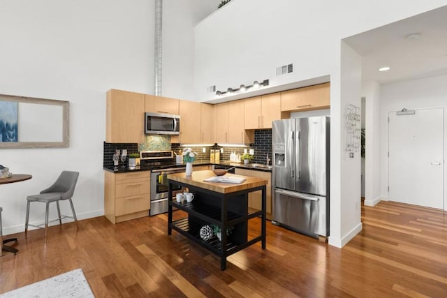 kitchen with a towering ceiling, appliances with stainless steel finishes, light brown cabinets, and dark hardwood / wood-style floors