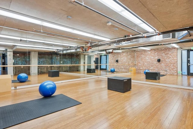 workout room with hardwood / wood-style flooring and brick wall