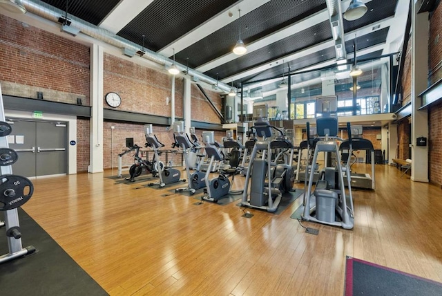 workout area with wood-type flooring, a high ceiling, and brick wall