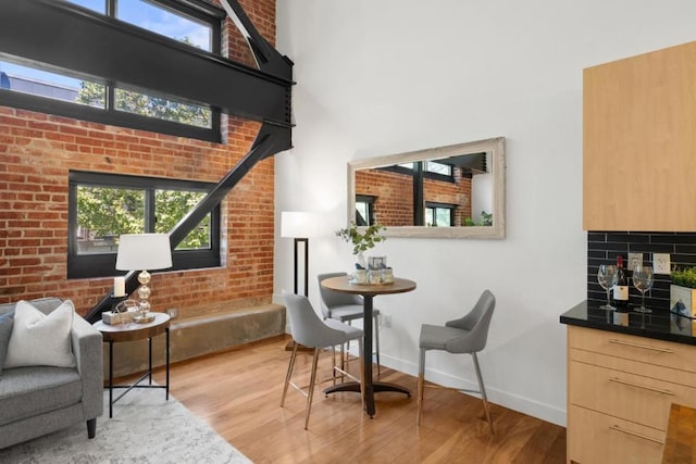 sitting room featuring a towering ceiling, light wood-type flooring, a healthy amount of sunlight, and brick wall