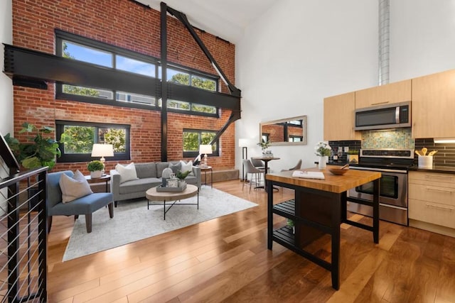 living room featuring brick wall, a high ceiling, and light hardwood / wood-style flooring