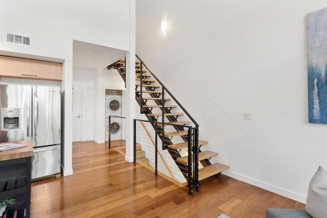 stairs with wood-type flooring and stacked washer / dryer