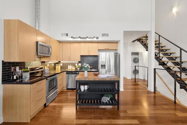 kitchen with stacked washer / dryer, light brown cabinetry, a towering ceiling, and stainless steel appliances