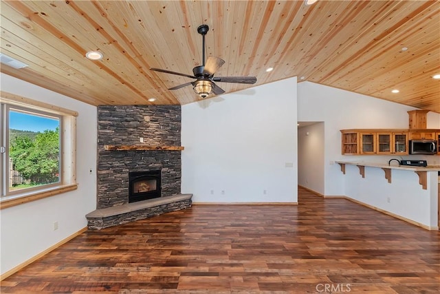 unfurnished living room with dark hardwood / wood-style floors, a stone fireplace, ceiling fan, and wooden ceiling