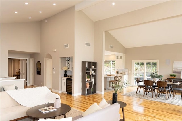 living room with wine cooler, beam ceiling, light wood-type flooring, and high vaulted ceiling