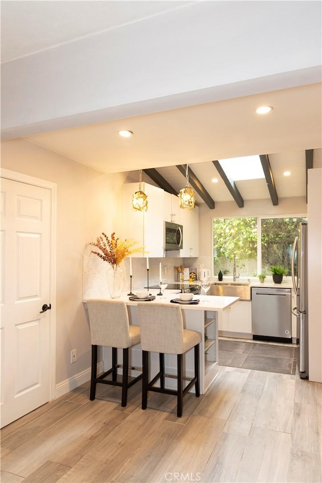 6829 Corintia St, Carlsbad, CA 92009 - kitchen with stainless steel appliances, a peninsula, white cabinets, a breakfast bar area, and beamed ceiling