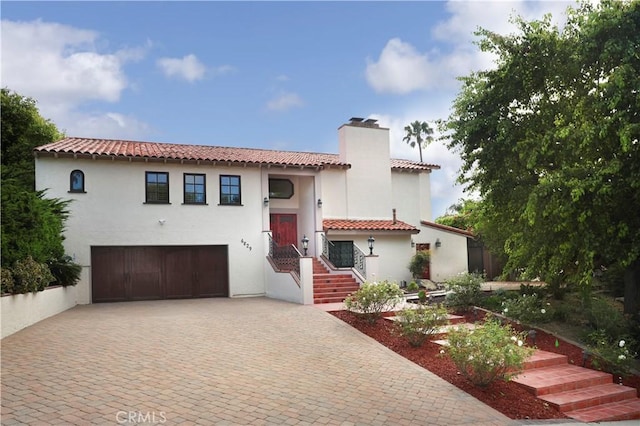 6829 Corintia St, Carlsbad, CA 92009 - mediterranean / spanish house featuring decorative driveway, a garage, a chimney, stucco siding, and a tiled roof