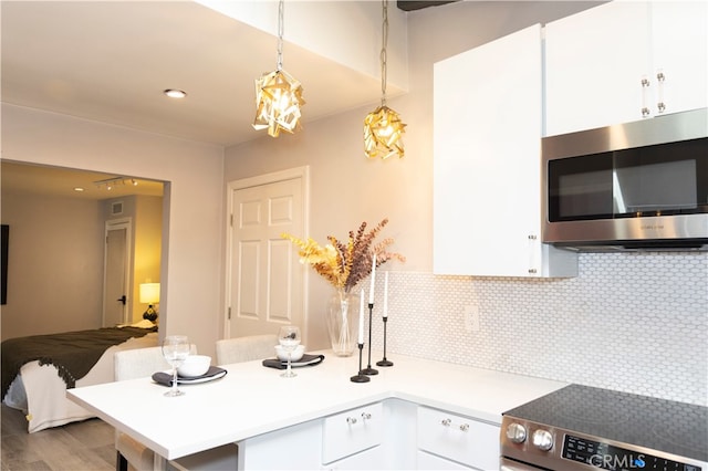 kitchen featuring pendant lighting, stove, white cabinets, hardwood / wood-style flooring, and decorative backsplash