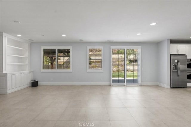 empty room featuring plenty of natural light, light tile patterned floors, and built in shelves