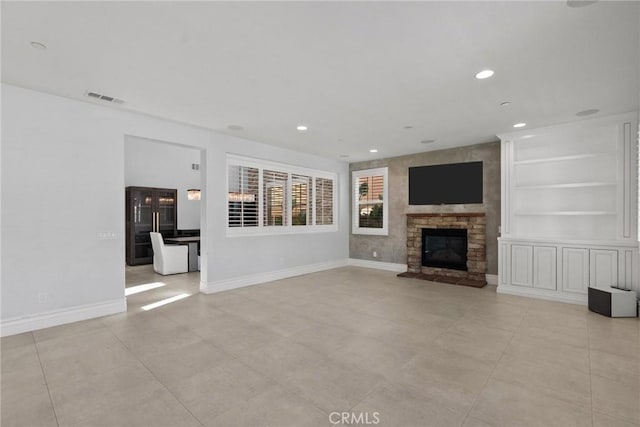 unfurnished living room with built in shelves, light tile patterned flooring, and a stone fireplace