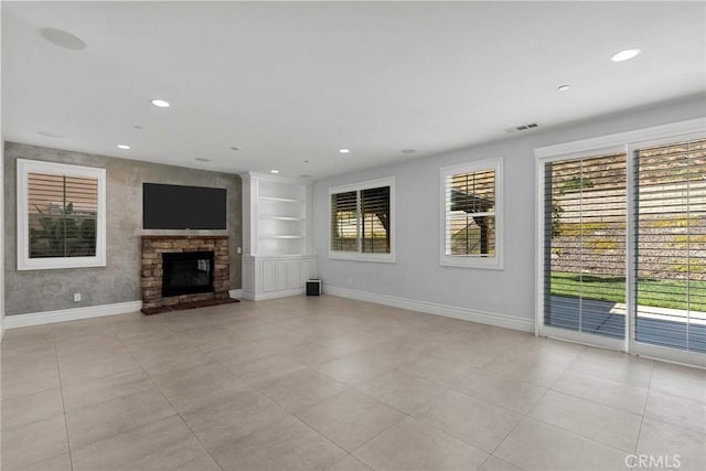 unfurnished living room with built in shelves, a stone fireplace, plenty of natural light, and light tile patterned floors