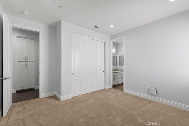 unfurnished bedroom with ensuite bath, light carpet, and a closet