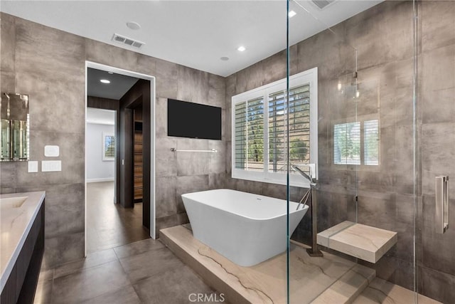 bathroom with concrete floors, vanity, independent shower and bath, and tile walls