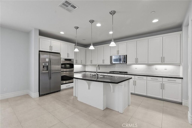 kitchen featuring white cabinets, appliances with stainless steel finishes, hanging light fixtures, and a kitchen island with sink