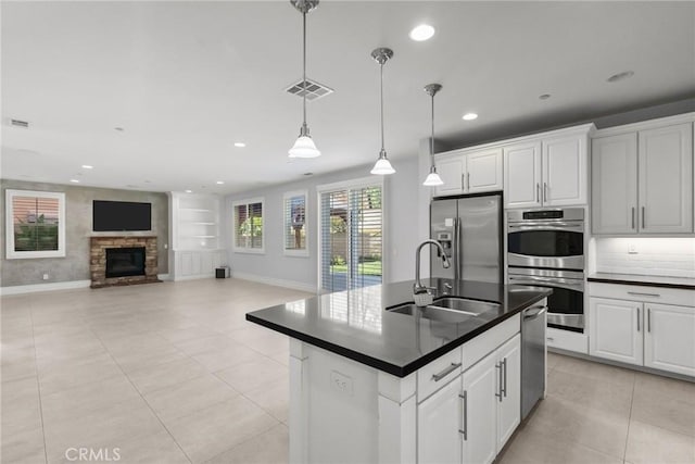 kitchen with white cabinets, a center island with sink, a stone fireplace, sink, and stainless steel appliances