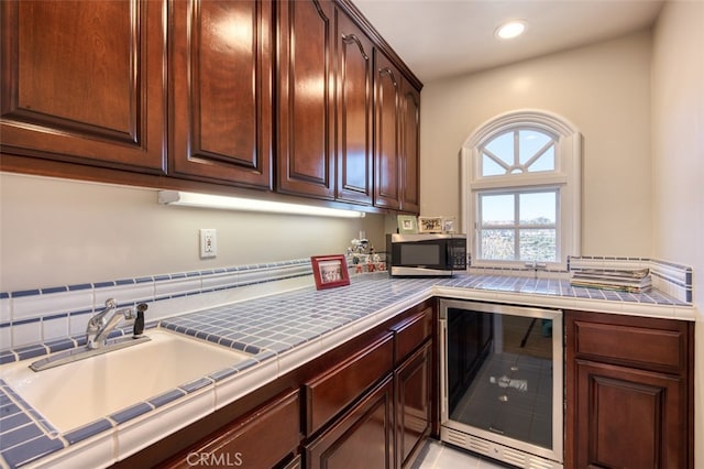 kitchen featuring tile counters, dark brown cabinetry, beverage cooler, and sink