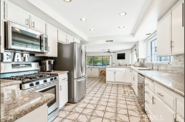 kitchen featuring light stone countertops, kitchen peninsula, stainless steel appliances, white cabinets, and decorative backsplash