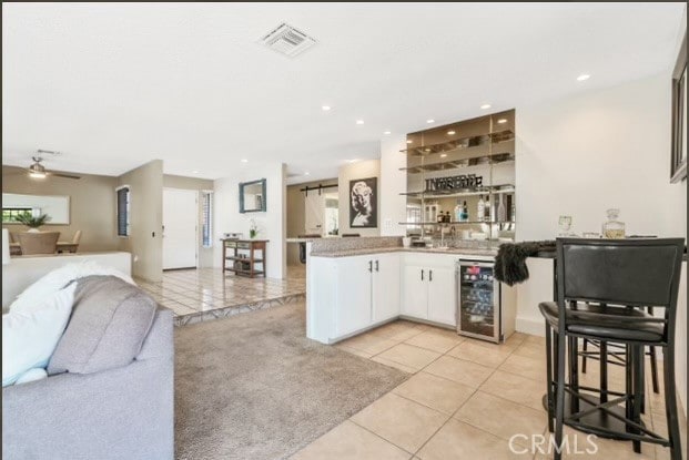 kitchen featuring beverage cooler, kitchen peninsula, ceiling fan, white cabinets, and light tile patterned floors