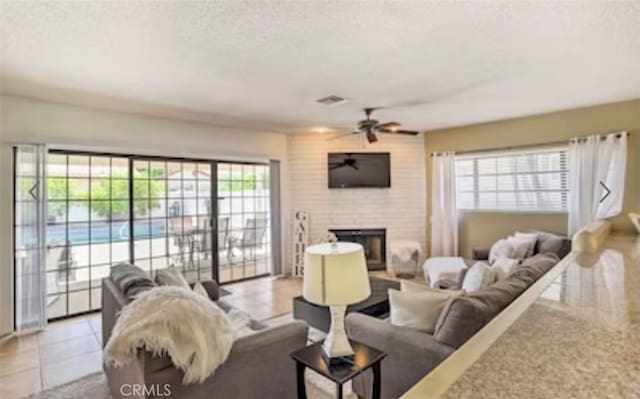 living room with a textured ceiling, light tile patterned floors, a large fireplace, and ceiling fan