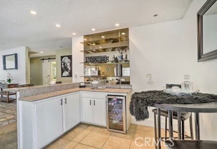 bar with wine cooler, a barn door, light tile patterned flooring, white cabinets, and a textured ceiling