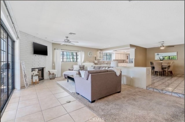 living room featuring a textured ceiling, ceiling fan, light tile patterned flooring, and a brick fireplace