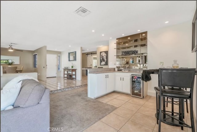 kitchen with kitchen peninsula, wine cooler, white cabinets, ceiling fan, and light tile patterned floors