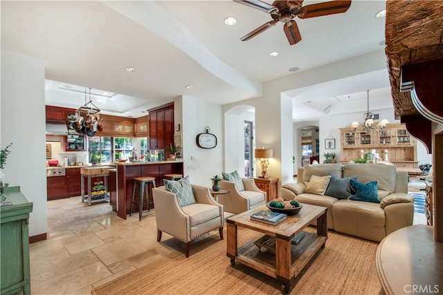 living room with ceiling fan with notable chandelier and a tray ceiling