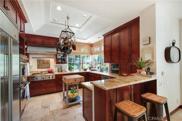 kitchen featuring pendant lighting, a kitchen breakfast bar, appliances with stainless steel finishes, a tray ceiling, and kitchen peninsula