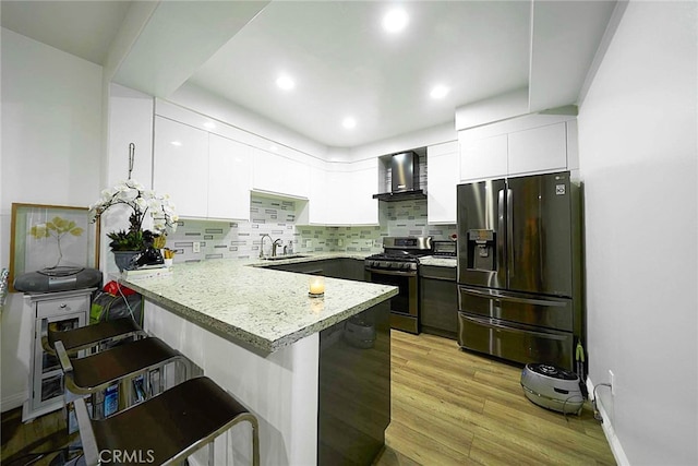 kitchen with appliances with stainless steel finishes, wall chimney exhaust hood, white cabinetry, and kitchen peninsula