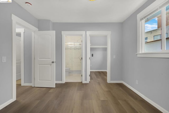 unfurnished bedroom with a closet, connected bathroom, hardwood / wood-style floors, and a walk in closet