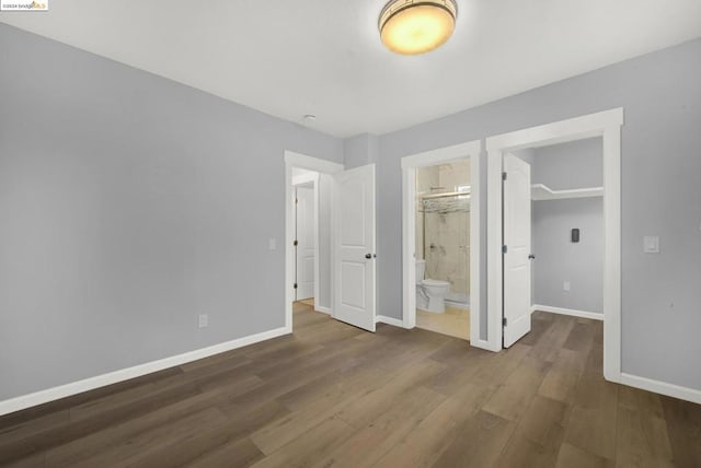 unfurnished bedroom featuring a closet, connected bathroom, dark wood-type flooring, and a walk in closet