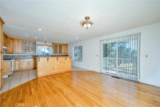 kitchen with a textured ceiling, light wood-type flooring, a breakfast bar, and white range