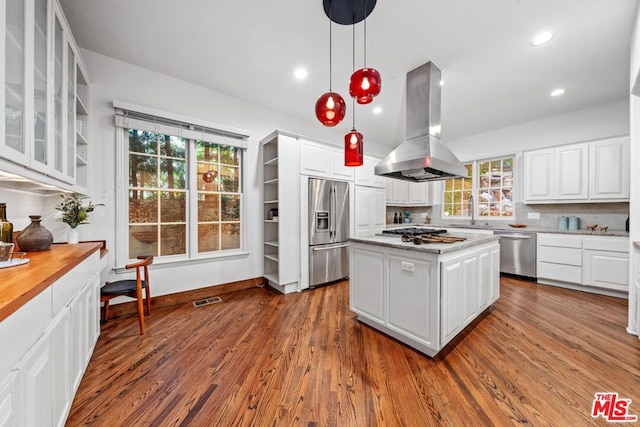 kitchen featuring hanging light fixtures, island range hood, white cabinetry, hardwood / wood-style flooring, and appliances with stainless steel finishes