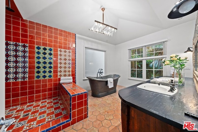 bathroom with tile walls, tile patterned flooring, vaulted ceiling, a tub to relax in, and vanity