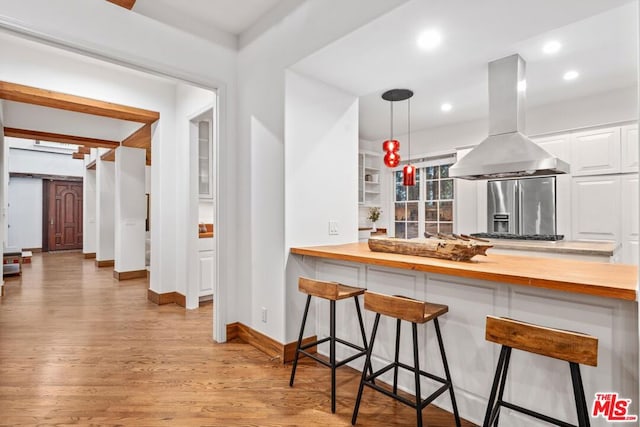 kitchen with wood counters, a breakfast bar area, white cabinets, island exhaust hood, and light hardwood / wood-style flooring