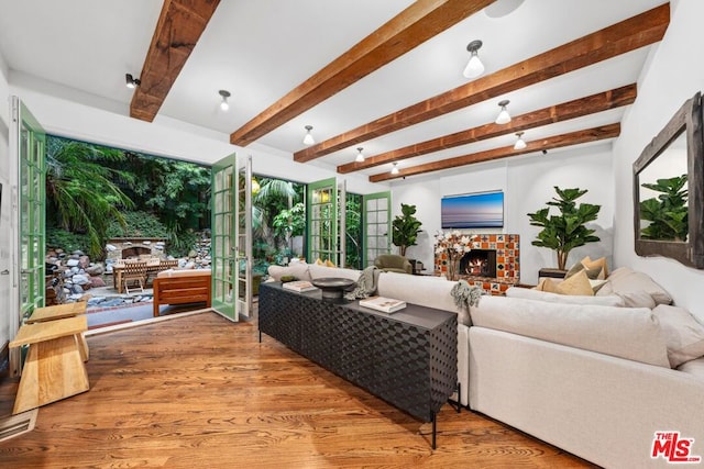 living room with a tile fireplace, beam ceiling, and wood-type flooring