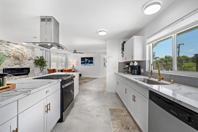 kitchen with a large fireplace, island range hood, stainless steel dishwasher, white cabinets, and sink