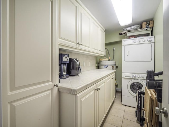 laundry room with stacked washer / dryer, light tile patterned floors, and cabinets