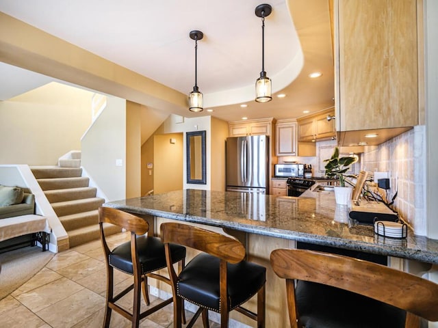 kitchen with stainless steel appliances, dark stone countertops, light brown cabinetry, hanging light fixtures, and kitchen peninsula