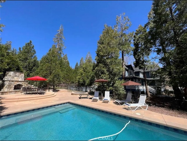 view of swimming pool featuring a patio and an outdoor stone fireplace