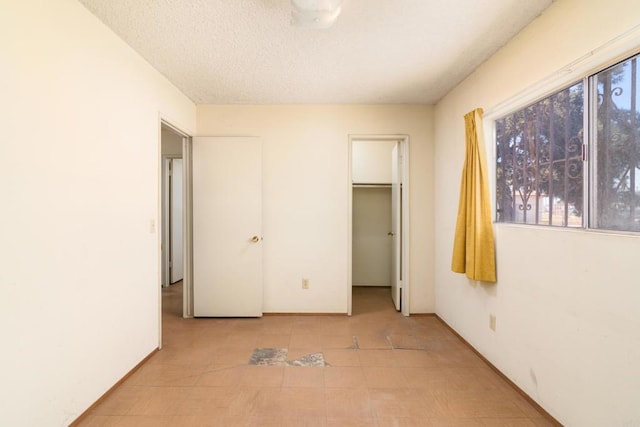 unfurnished bedroom featuring light tile patterned floors, a textured ceiling, a spacious closet, and a closet