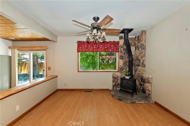 unfurnished living room featuring beam ceiling, ceiling fan, a wood stove, and hardwood / wood-style flooring