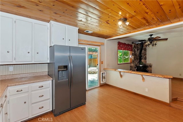 kitchen featuring stainless steel fridge, a wood stove, light hardwood / wood-style flooring, white cabinetry, and wooden ceiling