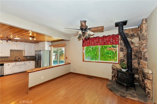 kitchen with beamed ceiling, sink, white cabinetry, stainless steel appliances, and light wood-type flooring